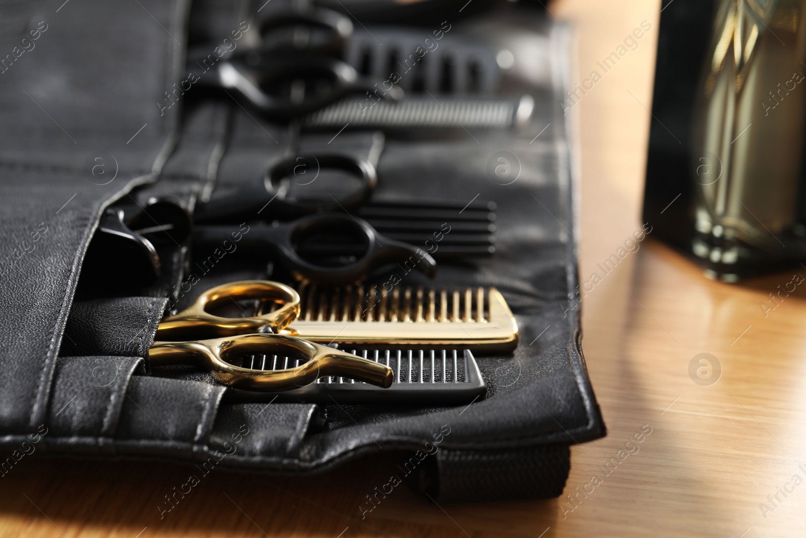 Photo of Hairdresser tools. Professional scissors and combs in leather organizer on wooden table, closeup