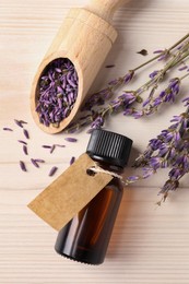 Bottle of essential oil and lavender flowers on white wooden table, flat lay