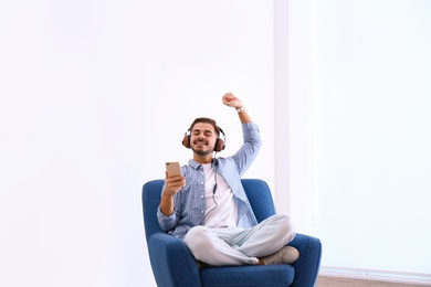 Handsome young man listening music in armchair indoors