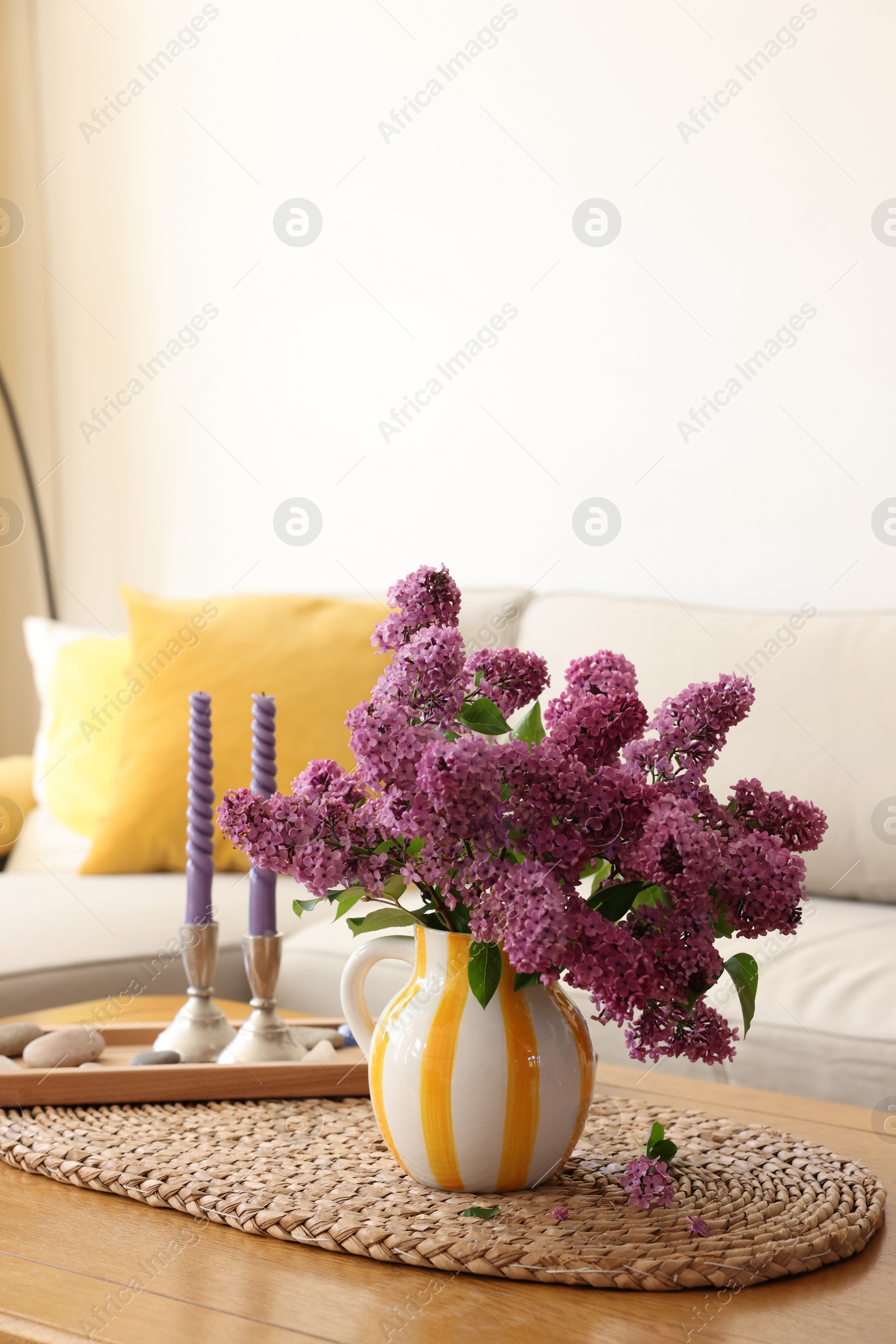 Photo of Beautiful fragrant lilac flowers in vase and candles on table at home