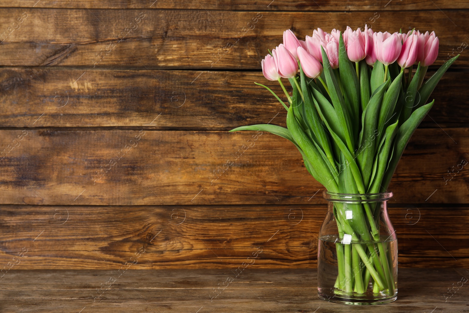 Photo of Beautiful pink spring tulips in vase on wooden table. Space for text