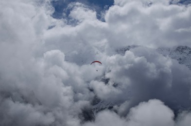 Paraglider flying in sky with fluffy clouds over mountains