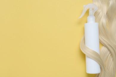 Photo of Spray bottle with thermal protection wrapped in lockblonde hair on yellow background, top view. Space for text