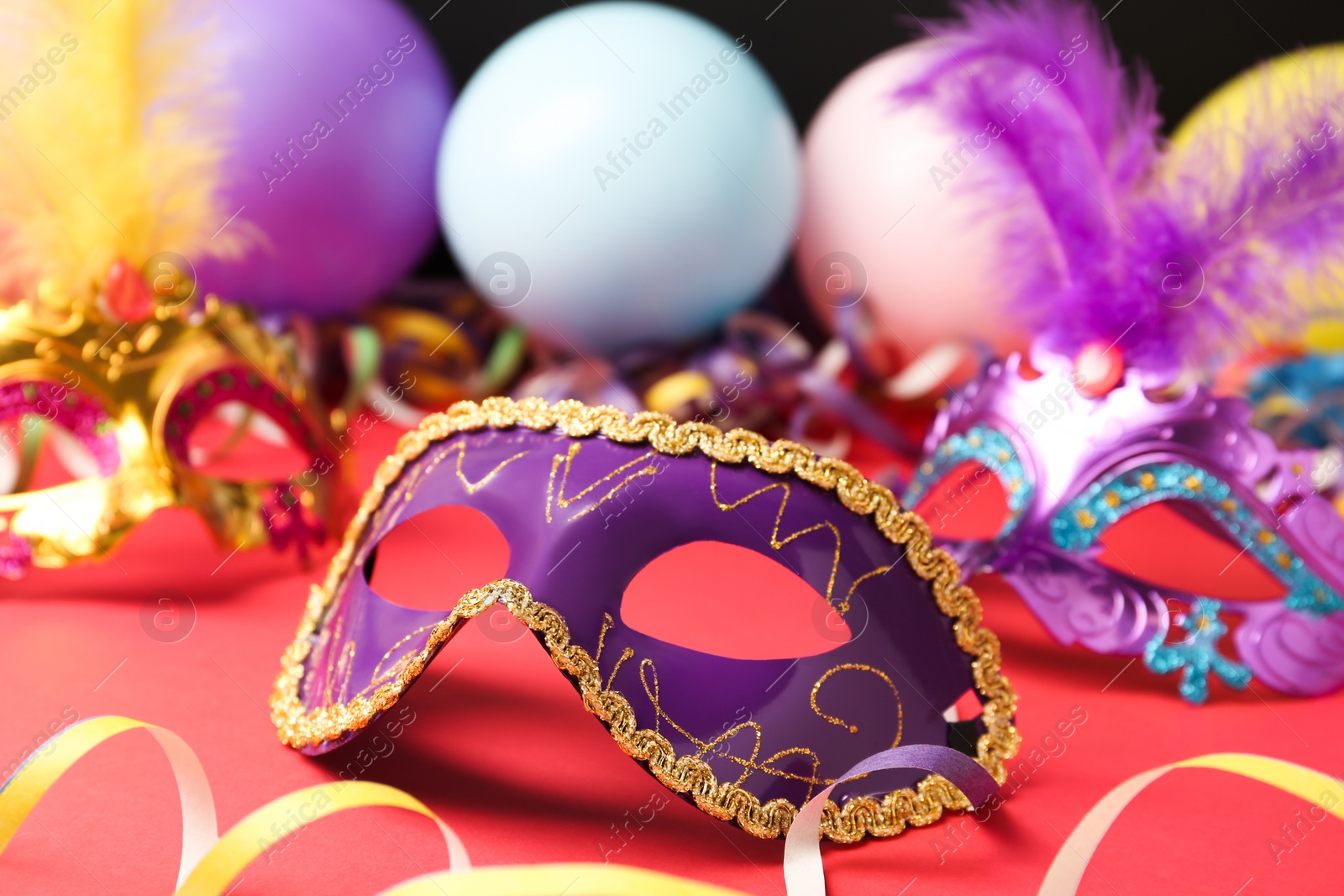 Photo of Beautiful carnival mask and party decor on red table, closeup