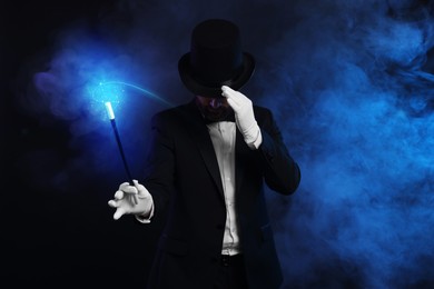 Image of Magic and sorcery. Magician with wand and fantastic light in smoke on dark background