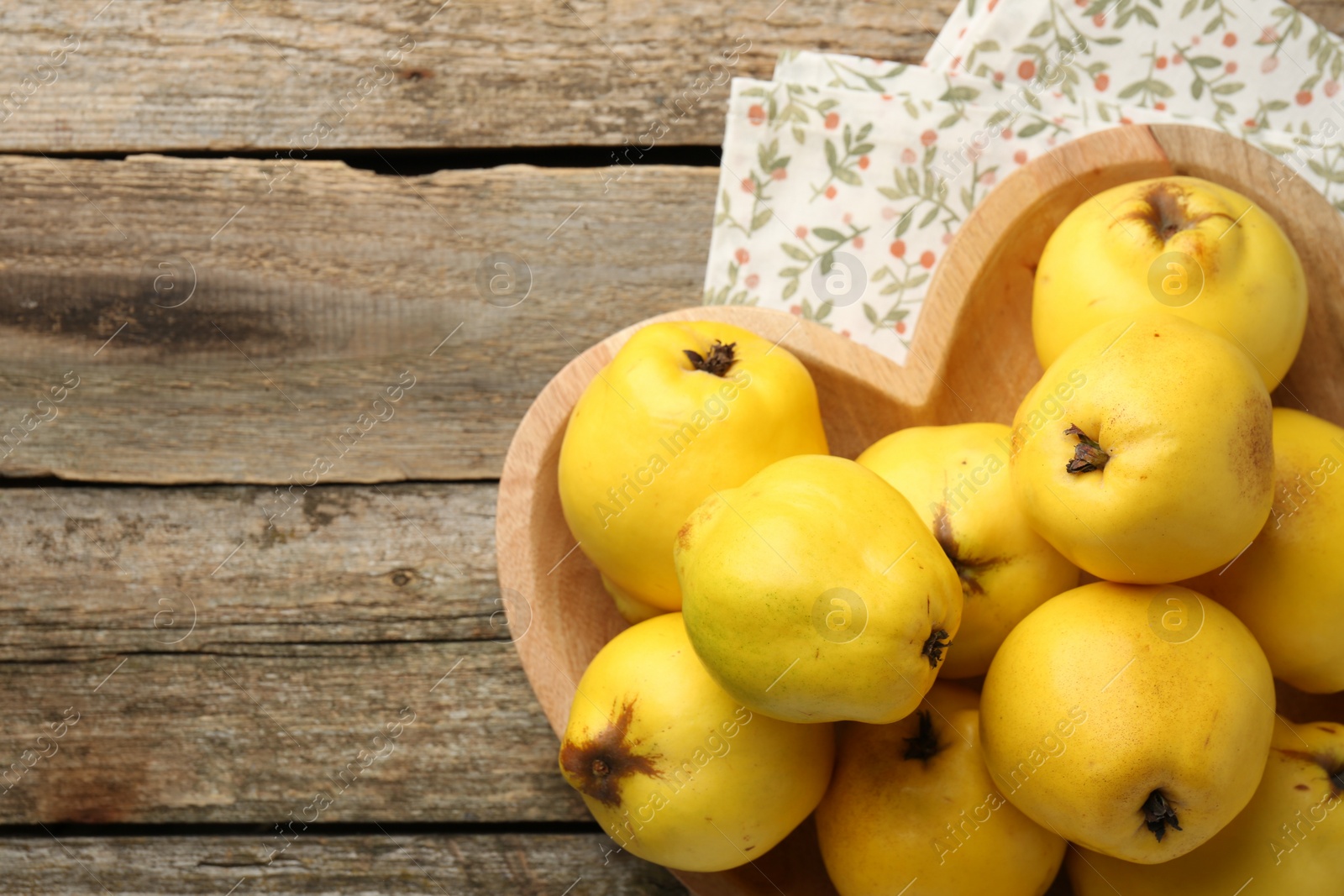 Photo of Tasty ripe quinces in heart shaped bowl on wooden table, top view. Space for text