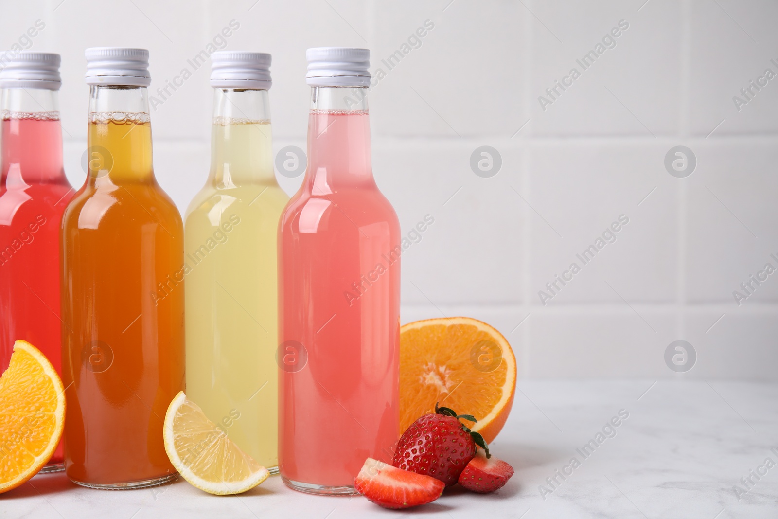 Photo of Delicious kombucha in glass bottles and fresh fruits on white marble table, space for text