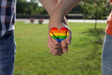 Image of Gay couple holding hands together in park on sunny day, closeup