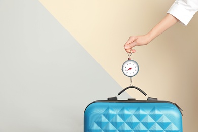 Woman weighing suitcase against color background, closeup. Space for text