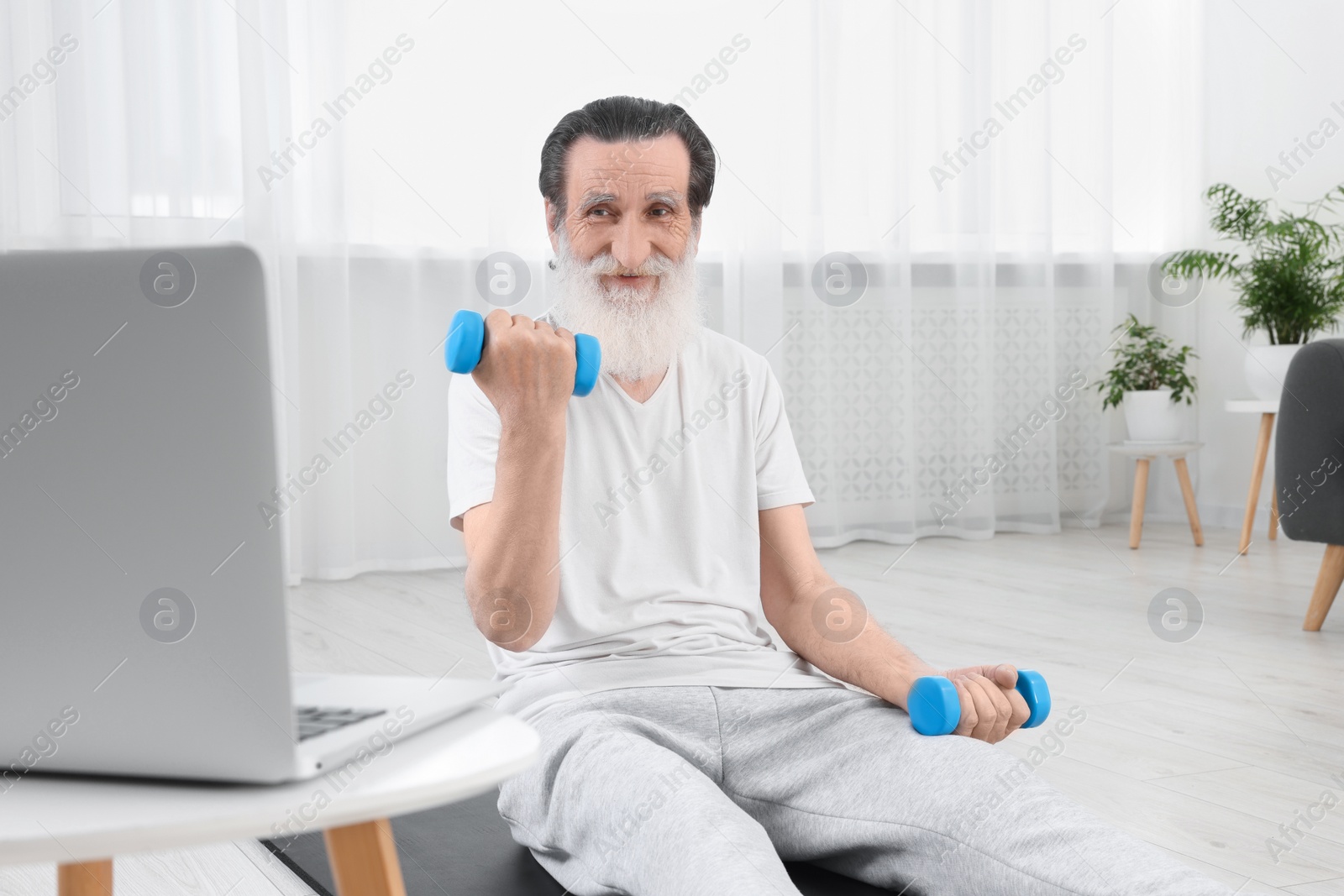 Photo of Senior man exercising with dumbbells while watching online tutorial at home. Sports equipment