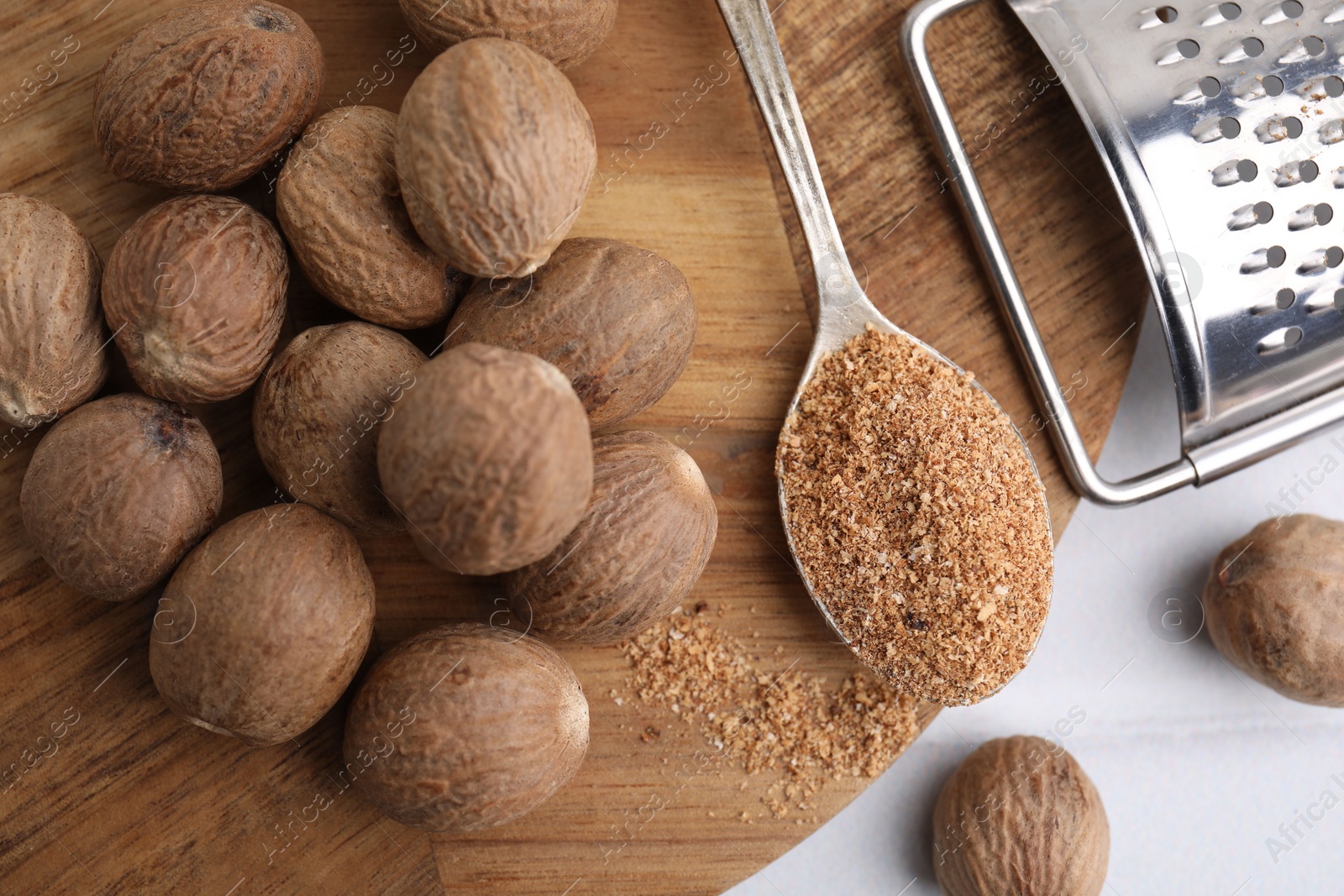 Photo of Spoon with grated nutmeg, seeds and grater on white table, flat lay