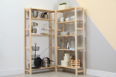 Photo of Wooden shelving units with kitchenware near color wall. Stylish room interior