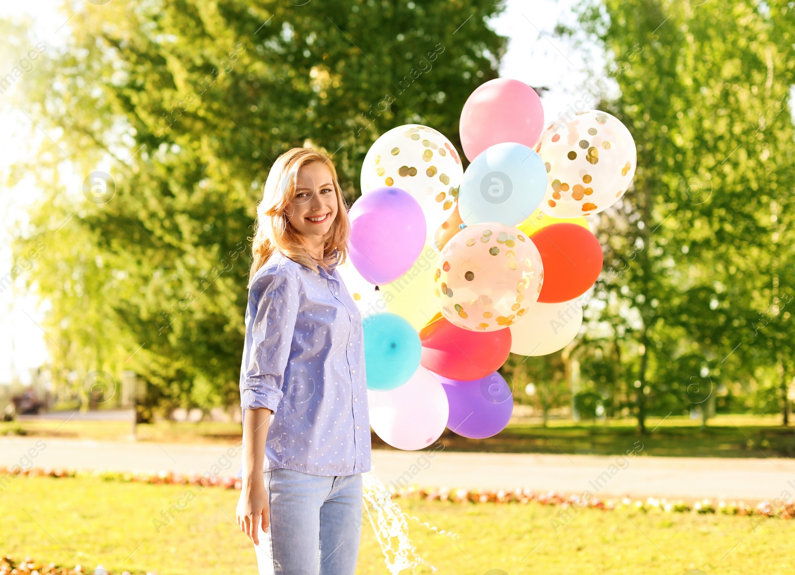 Photo of Young woman with colorful balloons outdoors on sunny day