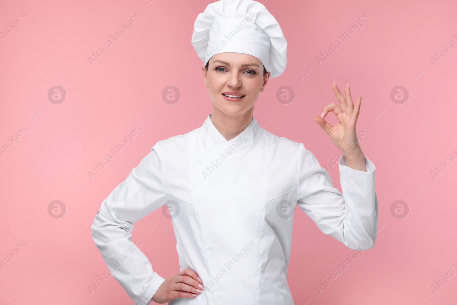 Photo of Happy chef in uniform showing OK gesture on pink background