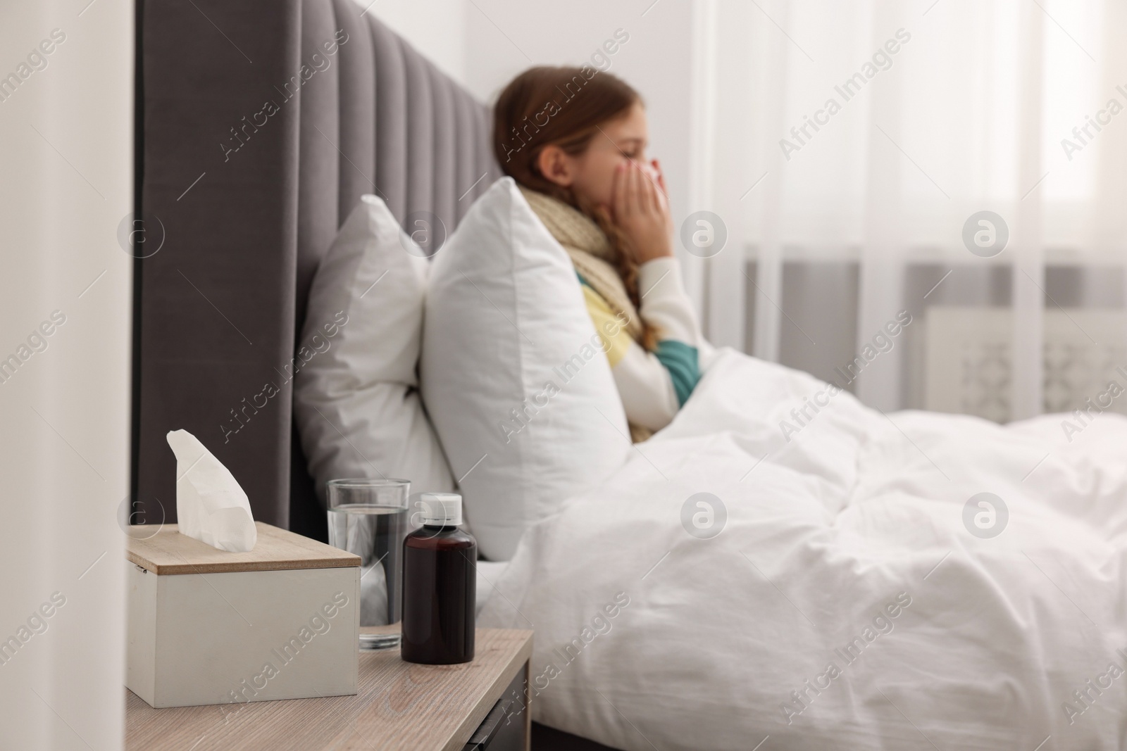 Photo of Sick girl with tissue coughing on bed at home, selective focus