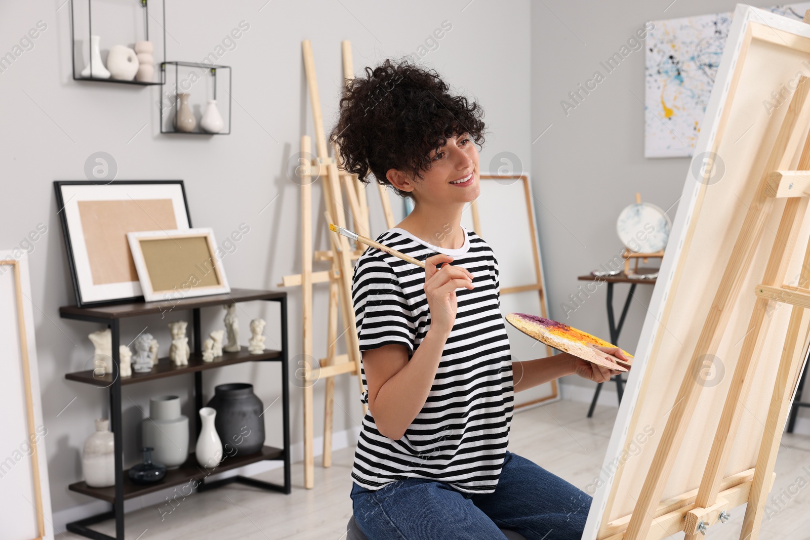 Photo of Young woman painting on easel with canvas in studio