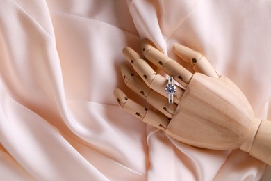 Elegant jewelry. Wooden mannequin hand with luxury ring on pink cloth, top view. Space for text