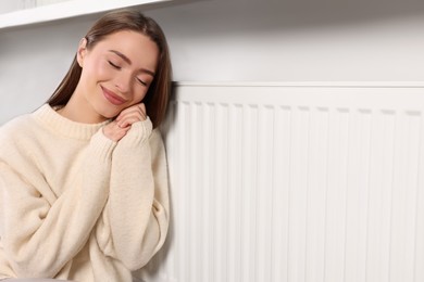 Young woman warming near heating radiator, space for text