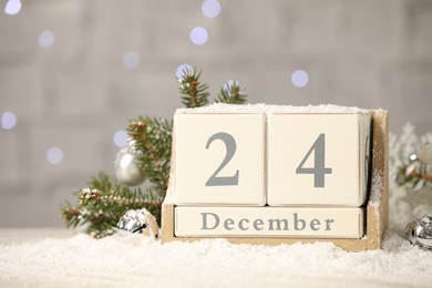 Photo of December 24 - Christmas Eve. Wooden block calendar and festive decor on snow against blurred lights
