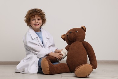 Little boy in medical uniform and toy bear with bandage indoors