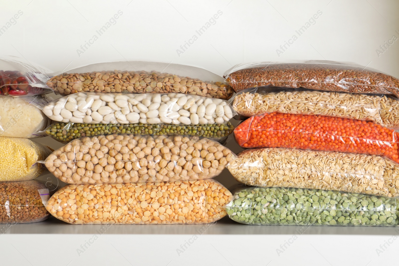 Photo of Different types of legumes and cereals in plastic bags on shelf. Organic grains