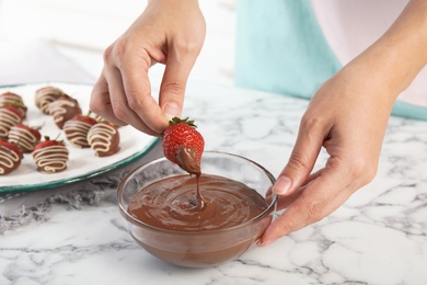 Photo of Woman dipping ripe strawberry into bowl with melted chocolate on table