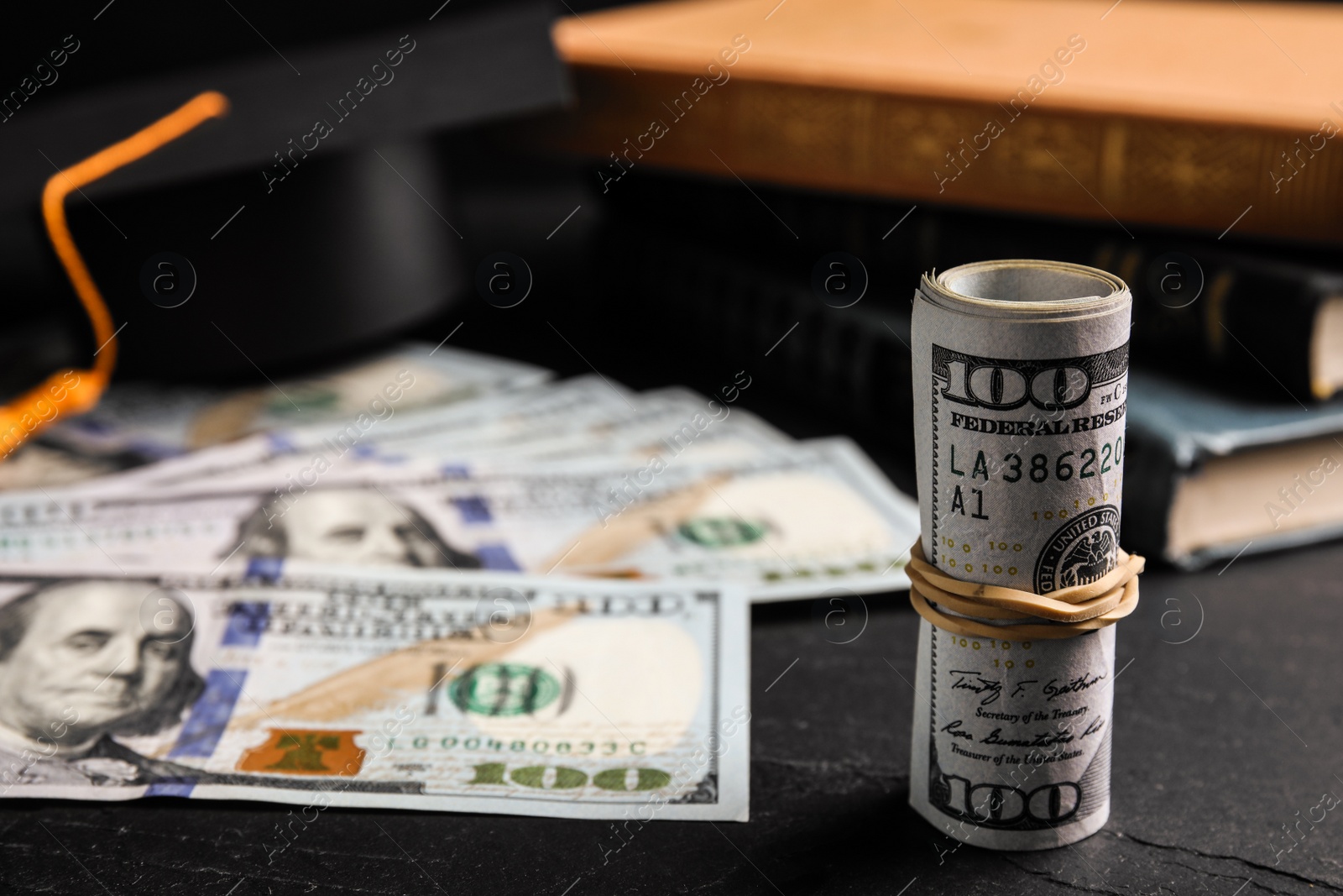 Photo of Dollar banknotes, student graduation hat and books on black table. Tuition fees concept