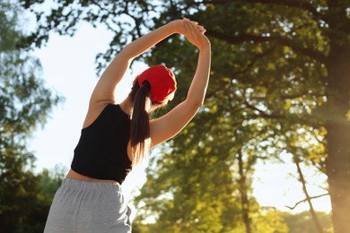 Photo of Young woman doing morning exercise in park, back view. Space for text