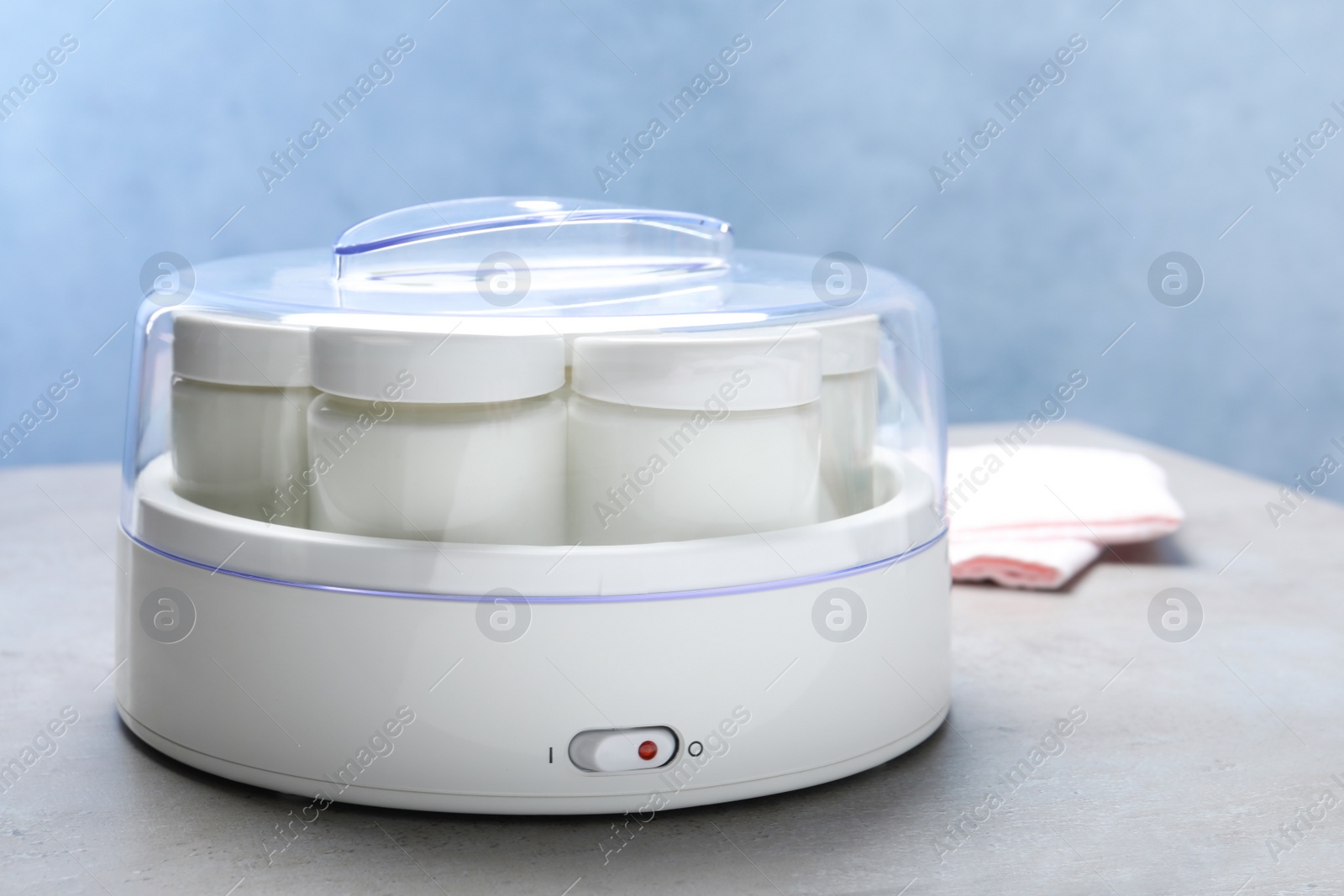 Photo of Modern yogurt maker with full jars on grey table