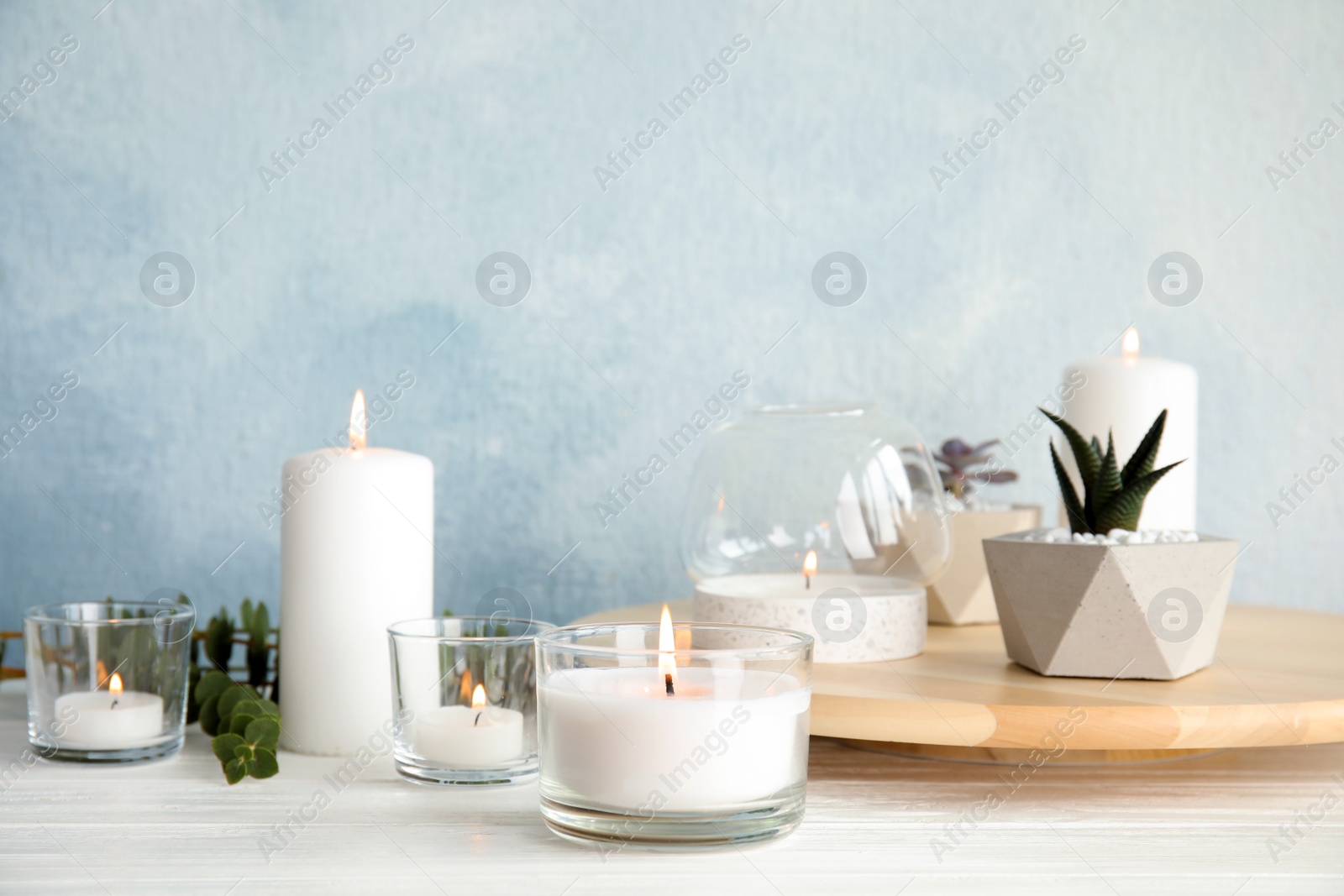 Photo of Burning aromatic candle and plants on table. Space for text