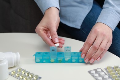 Woman taking pill from plastic container at white table indoors, closeup