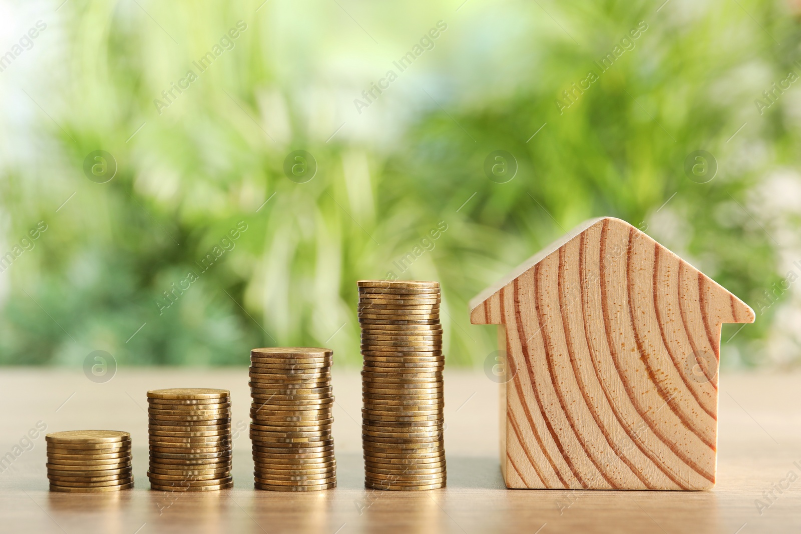 Photo of Mortgage concept. Model house and stacks of coins on wooden table against blurred green background, closeup