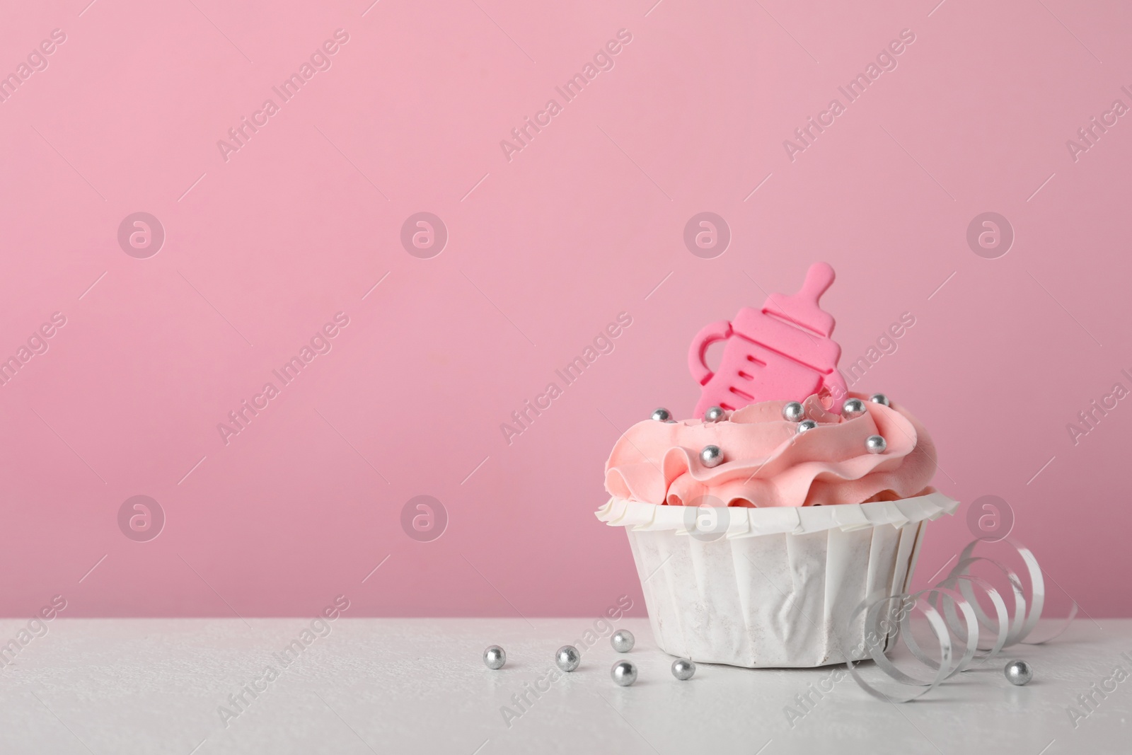 Photo of Baby shower cupcake with topper on white table against pink background, space for text