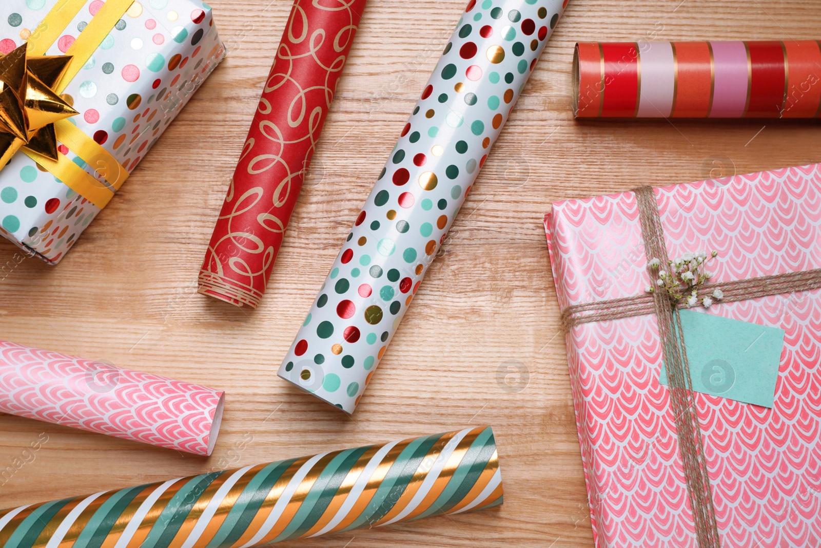 Photo of Different colorful wrapping paper rolls and gift boxes on wooden table, flat lay