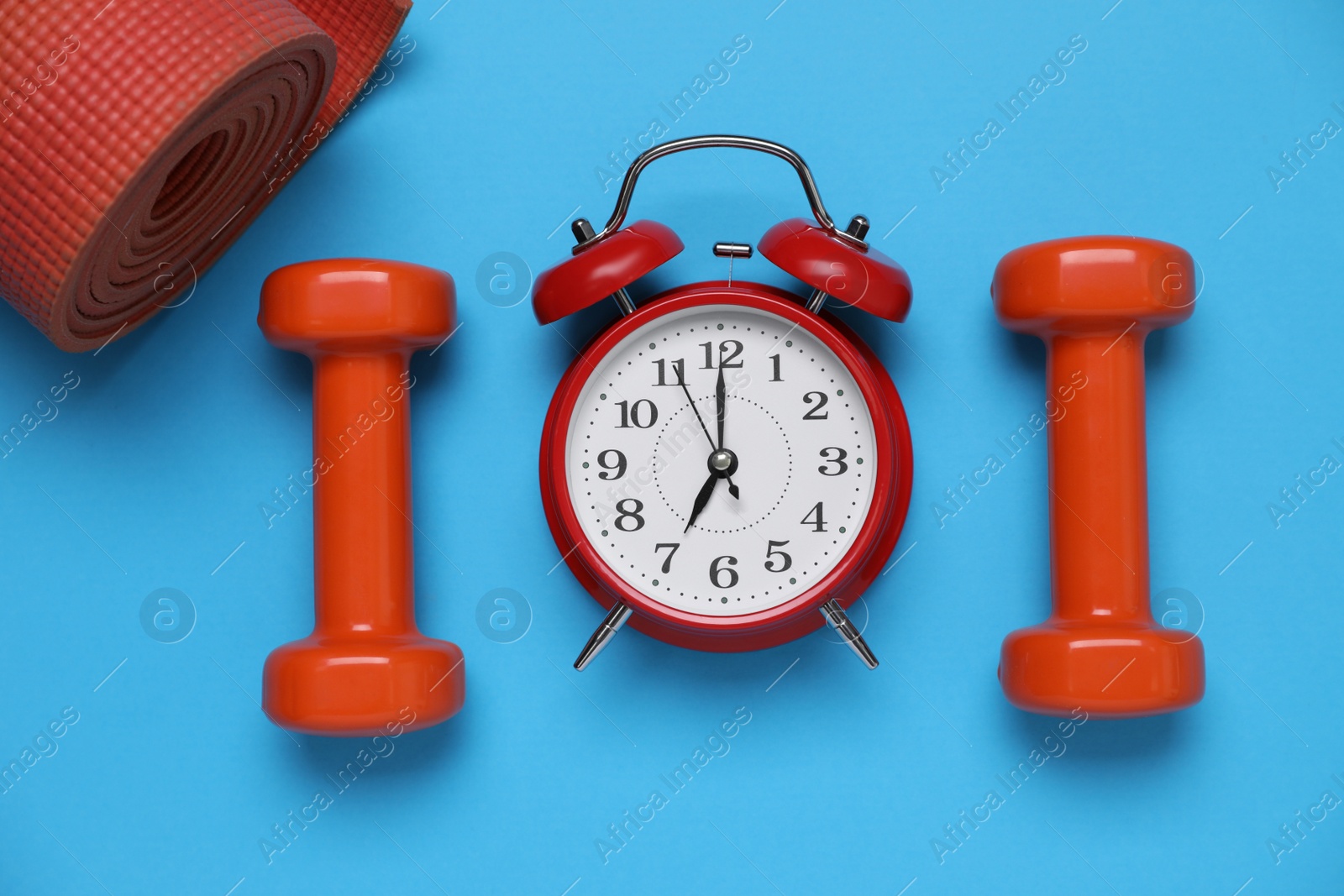 Photo of Alarm clock, dumbbells and yoga mat on light blue background, flat lay. Morning exercise