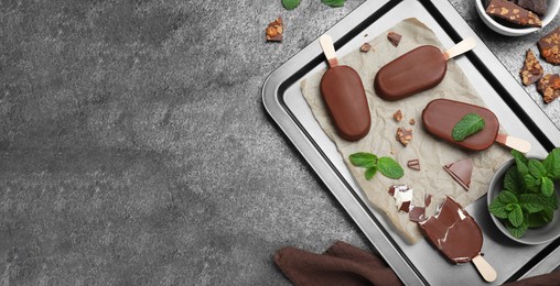 Flat lay composition with glazed ice cream bars, fresh mint and chocolate on grey table, space for text. Banner design