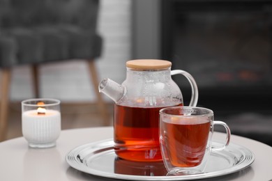 Teapot, cup of aromatic tea and burning candle on white table indoors, space for text