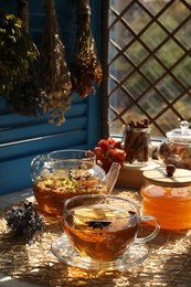 Aromatic tea, different dry plants and honey on table near window