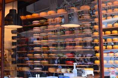 Photo of Amsterdam, Netherlands - June 25, 2022: Many cheese wheels on shelves, view through glass window