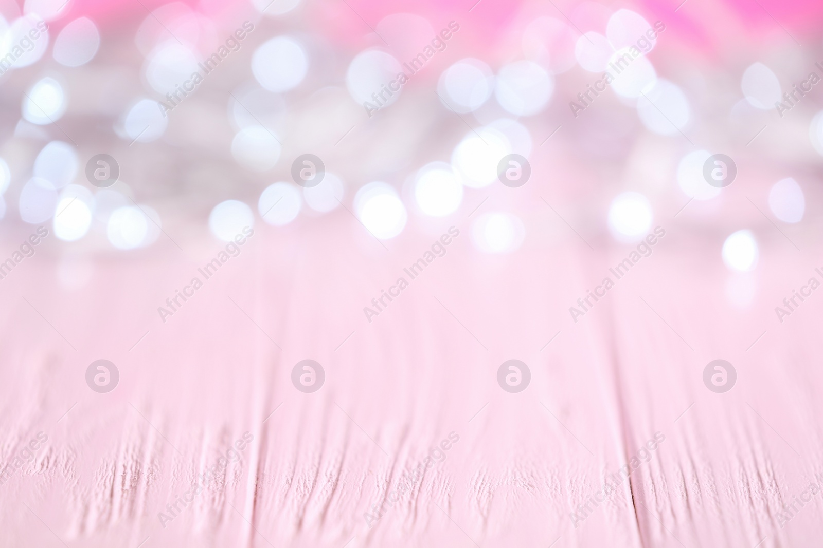 Photo of White Christmas lights on pink wooden table, blurred view