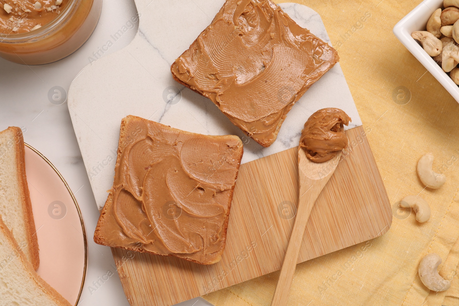 Photo of Toasts with tasty nut butter and cashews on white marble table, flat lay