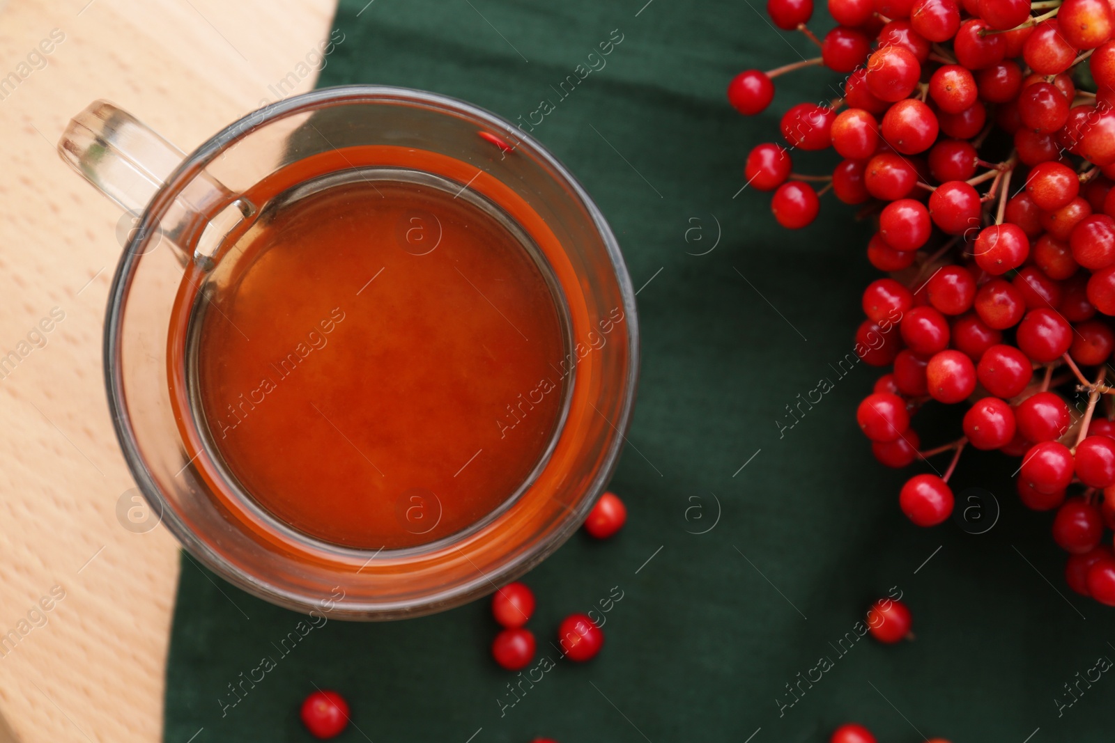 Photo of Cup of tea and fresh ripe viburnum berries on wooden table, flat lay