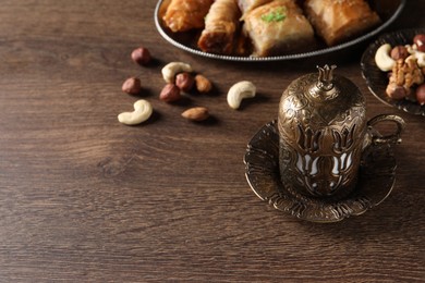 Photo of Beautiful vintage cup holder, nuts and baklava dessert on wooden table, space for text