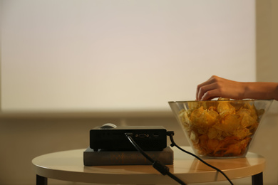 Photo of Woman eating chips while watching movie using video projector at home, closeup