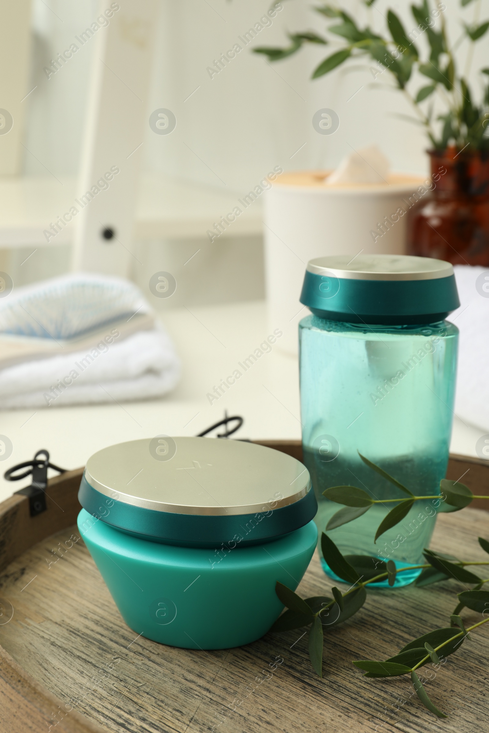 Photo of Hair care cosmetic products and green leaves on wooden tray indoors