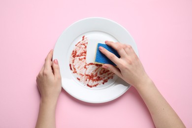 Woman washing dirty plate with sponge on pink background, top view