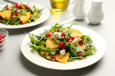 Delicious persimmon salad with pomegranate and arugula served on light grey table