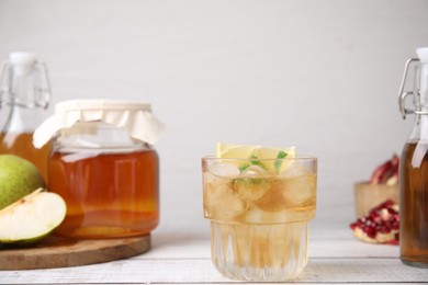 Tasty kombucha and ice cubes in glass on white wooden table