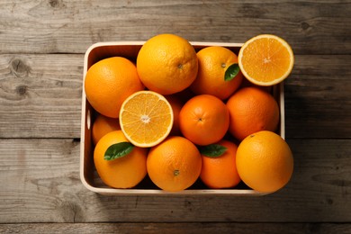 Photo of Many whole and cut ripe oranges on wooden table, top view