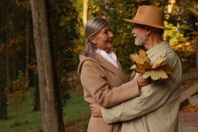 Photo of Affectionate senior couple with dry leaves in autumn park, space for text
